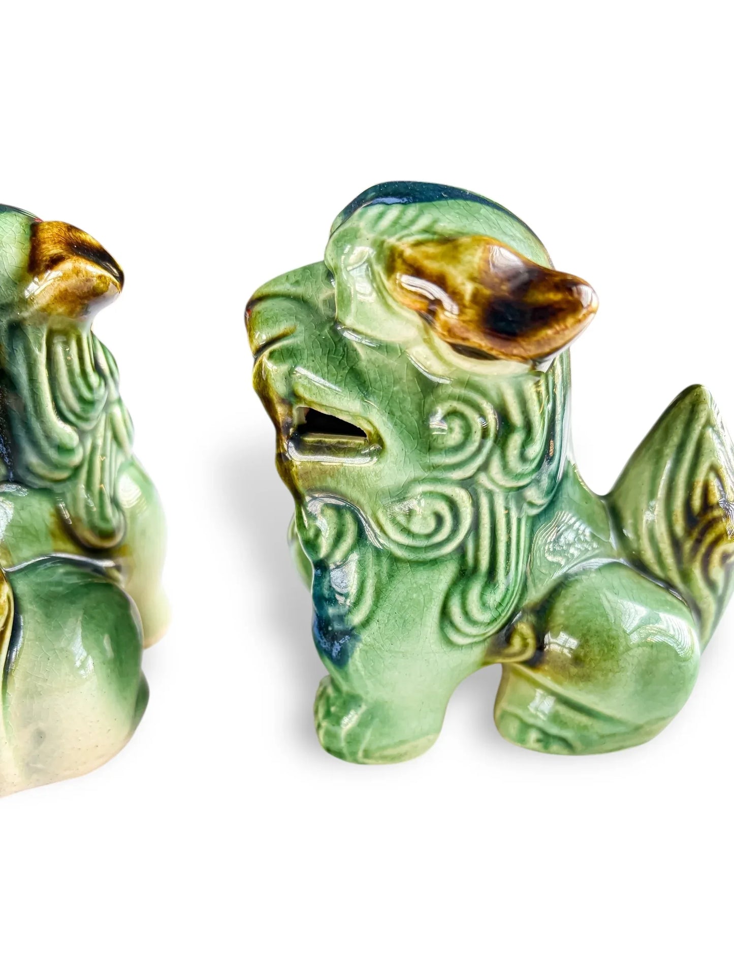 Glossy green ceramic Foo dog figurines with intricate swirling patterns and brown accents