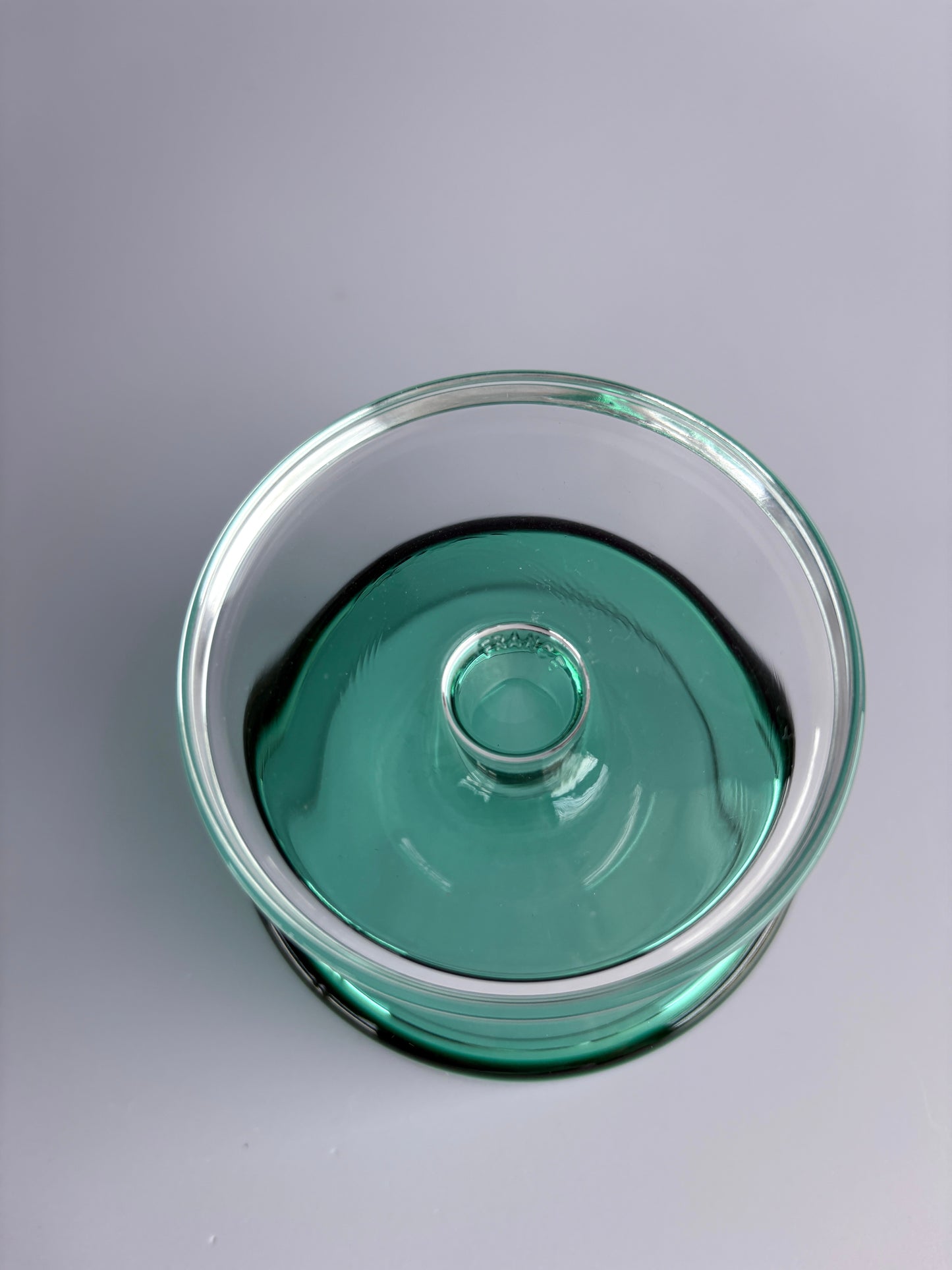 Top view of a clear green glass dish or bowl with a central raised circular detail on a white background