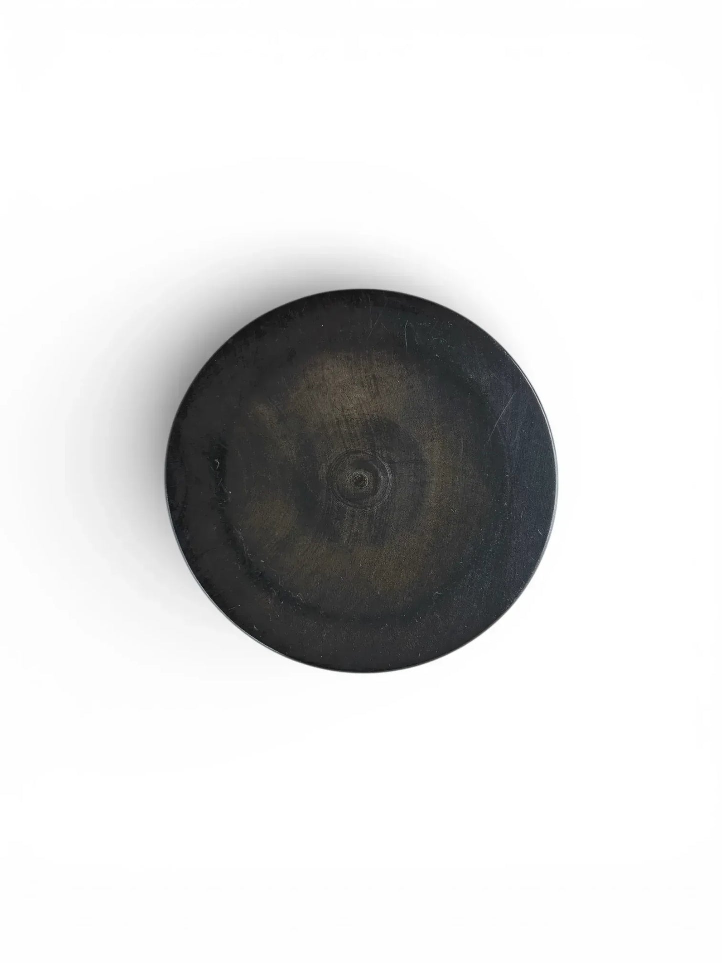 The underside of an ebonised turned wood box, showing circular grain patterns and subtle hints of the lighter natural wood beneath the black finish.