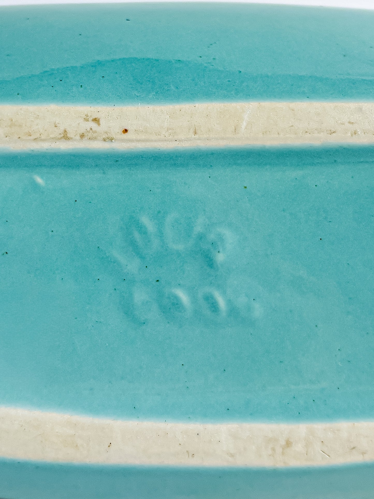 Close-up of turquoise ceramic piece with embossed maker's mark and unglazed foot ridge