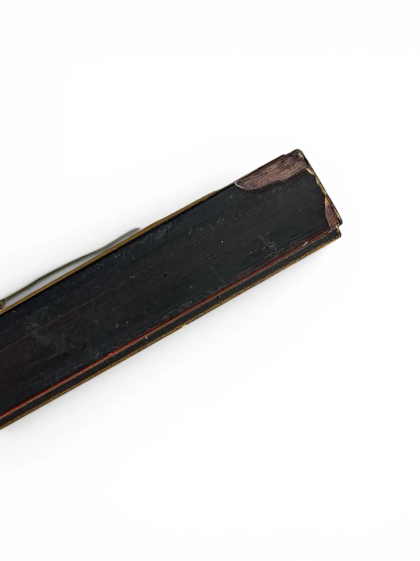 A close-up profile shot of the long side of a vintage wooden frame profile isolated on a clean white background. The dark, distressed lacquer backing is visible alongside thin gold and red trim lines along the decorative front lip.
