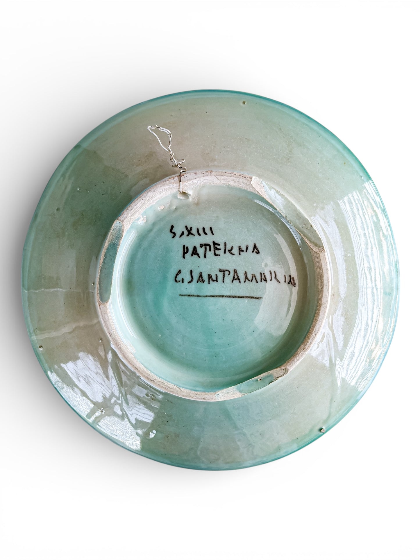 Bottom view of vintage turquoise glazed ceramic plate with handwritten markings and wire hanger