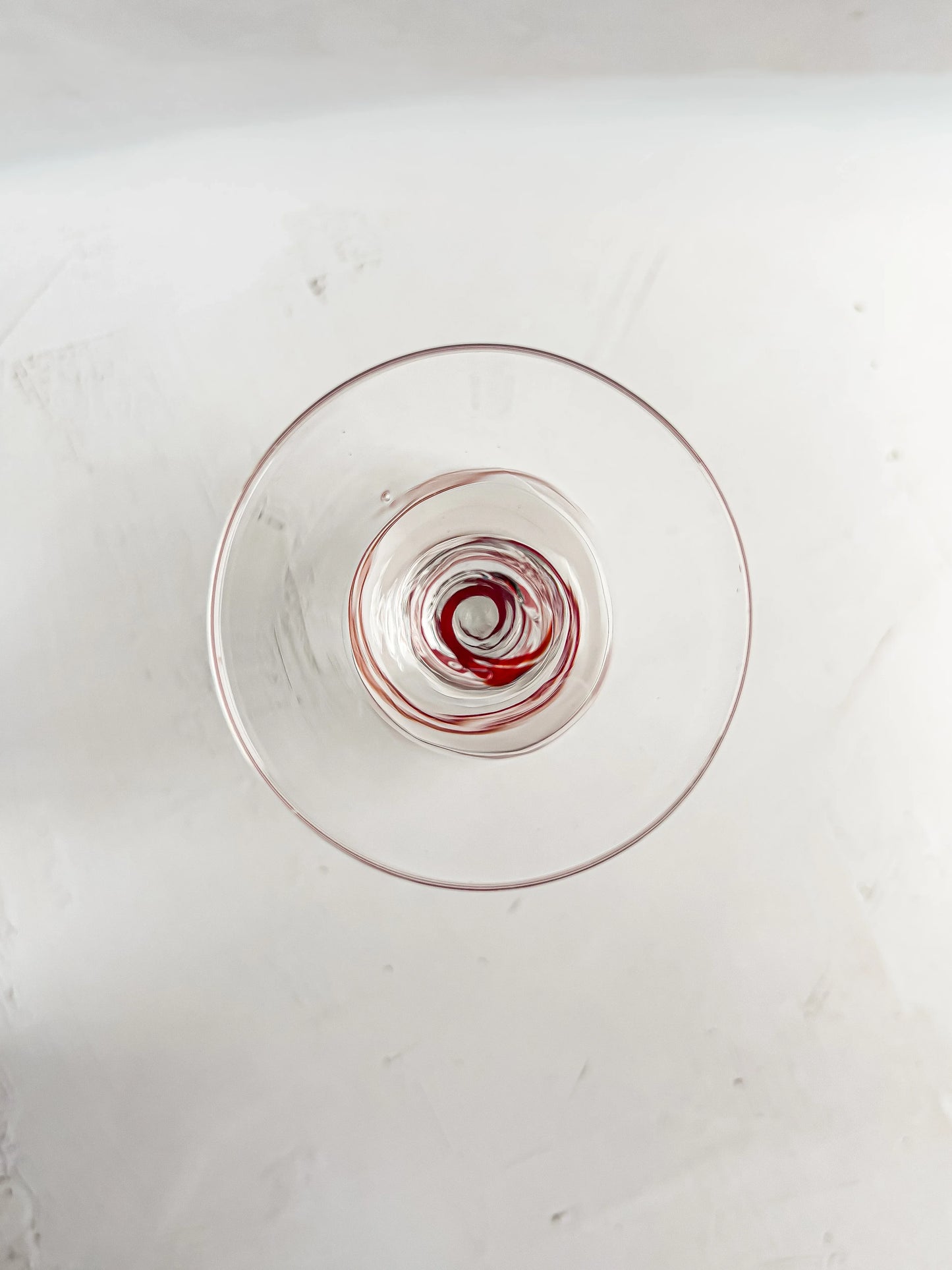 Top view of a clear glass with red wine residue swirled at the bottom on a white surface