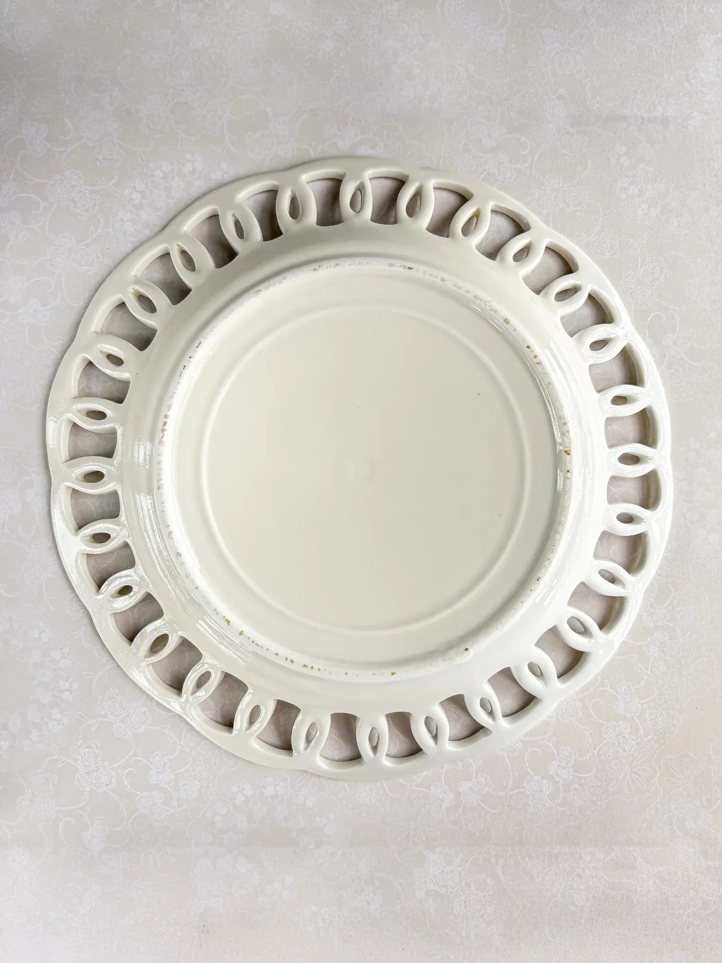White ceramic decorative plate with cutout looped edge design on floral tablecloth