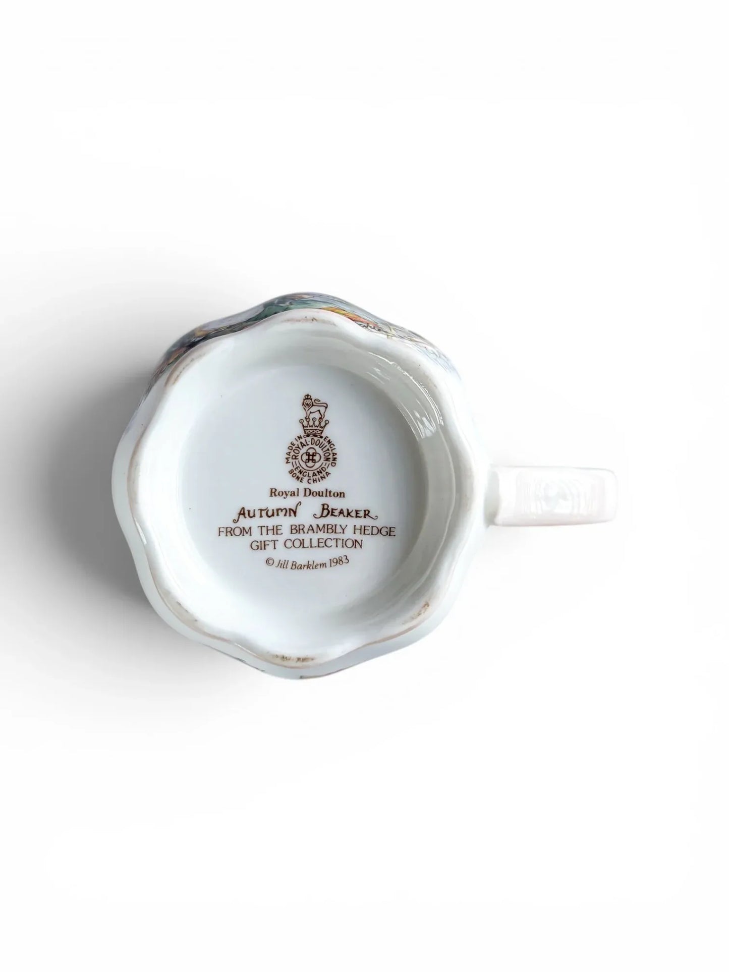 Close-up of the underside of the Royal Doulton Autumn beaker, showing the official brown backstamp with the Lion and Crown crest, "Made in England," and the 1983 copyright date for Jill Barklem and the Brambly Hedge Gift Collection.
