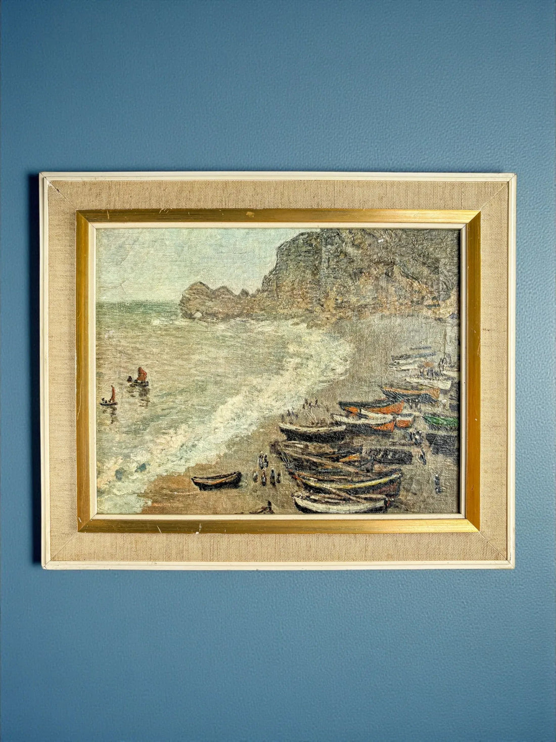  Vintage coastal oil painting depicting boats on the shore, rocky cliffs, and shoreline waves in soft muted tones.