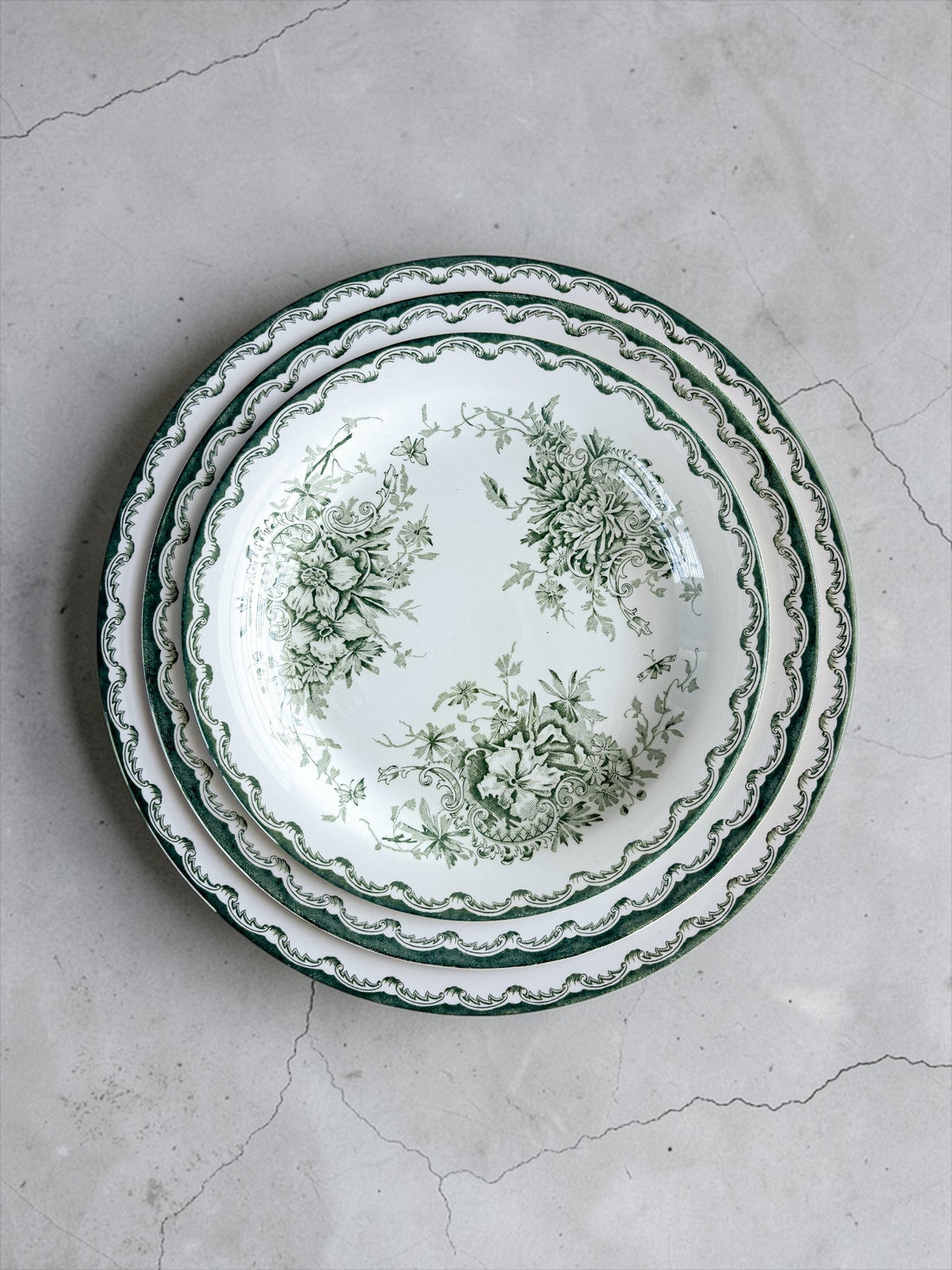 A stack of three Rörstrand Grön Anna vintage plates—including the 23.9 cm dinner plate, 21 cm salad plate, and 17.9 cm bread plate—showing the iconic green floral border against a cream-white flintware surface, photographed on a concrete background