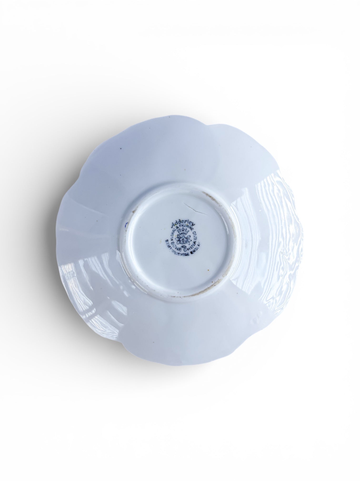 Back of a white Adderley fine bone china saucer with scalloped edges and maker's mark on a white background