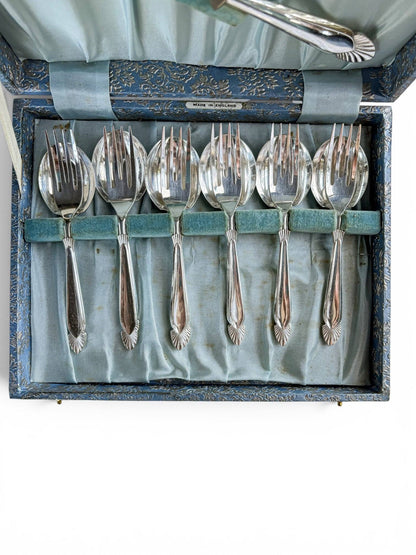 Close-up view of six vintage silver-plated dessert forks neatly nested over matching dessert spoons within a pale blue velvet slot tray inside an original vintage presentation box.