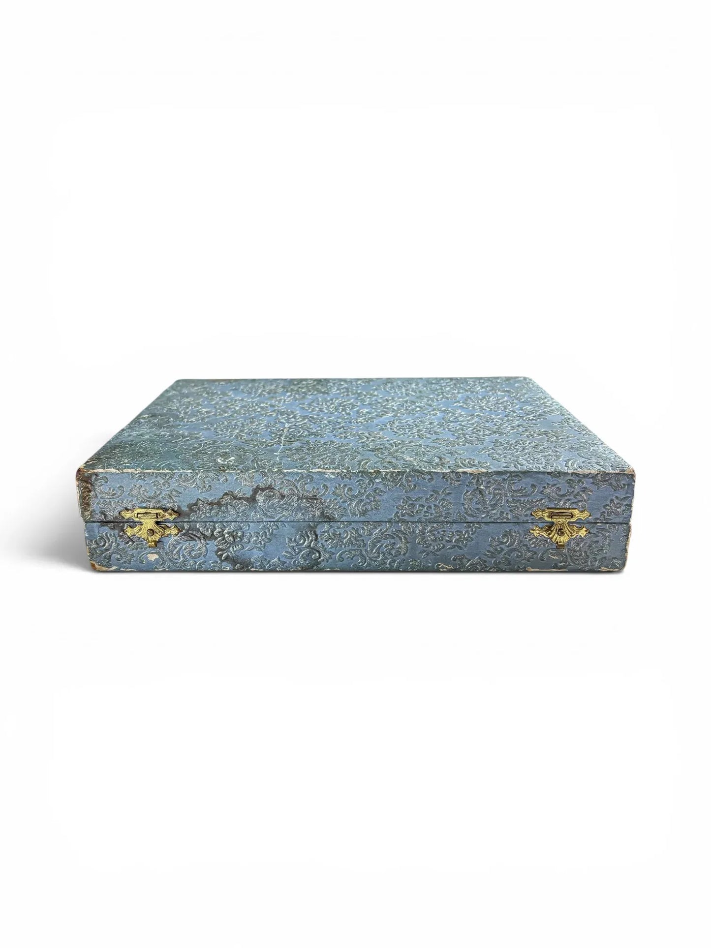 Front view of a vintage closed blue embossed damask presentation case for cutlery, showing age-authentic wear along the edges and two vintage brass-toned latches.