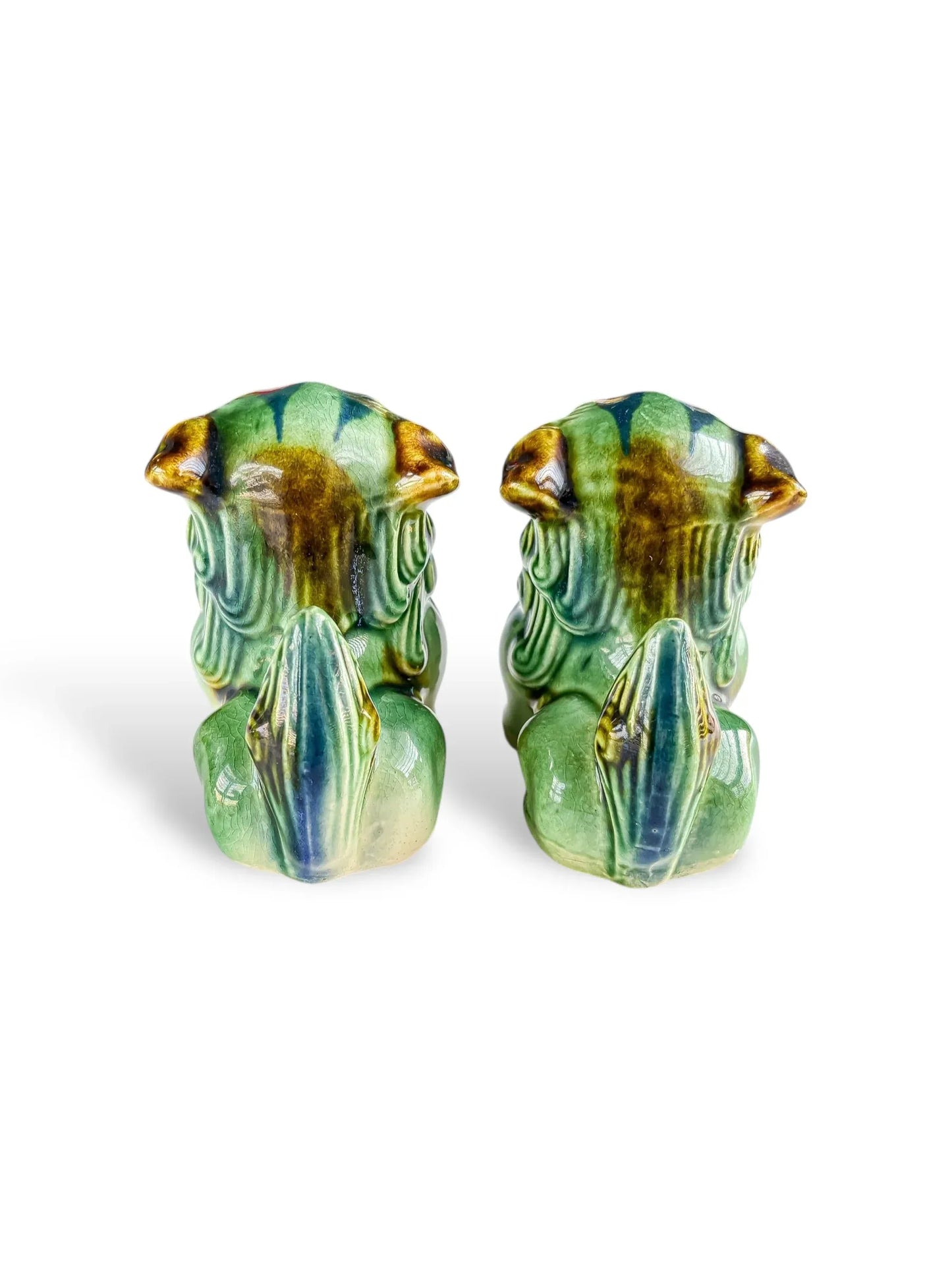 Pair of green and brown ceramic frog figurines viewed from behind on a white background