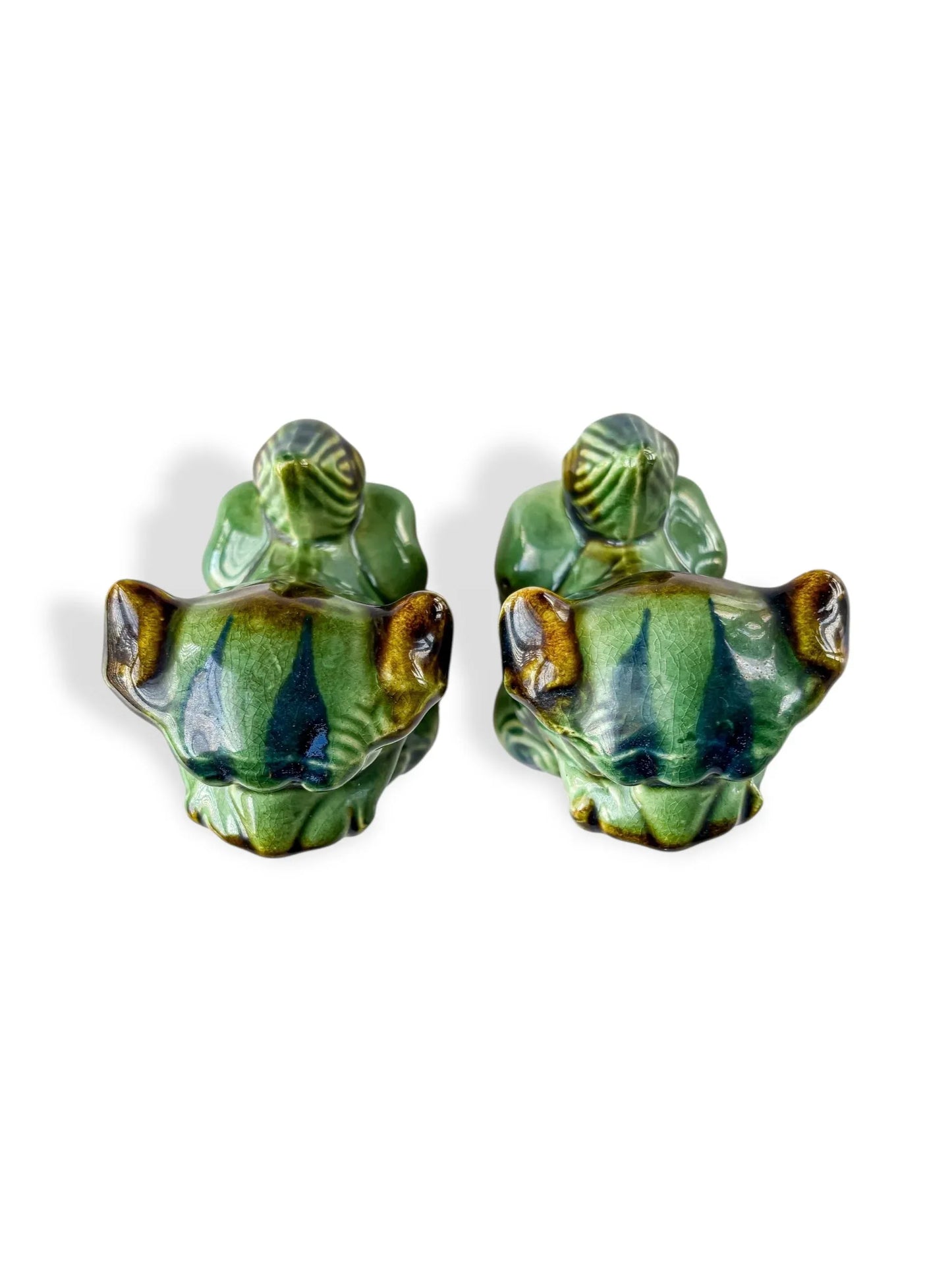 Pair of green ceramic frog figurines with brown and blue glaze accents on white background