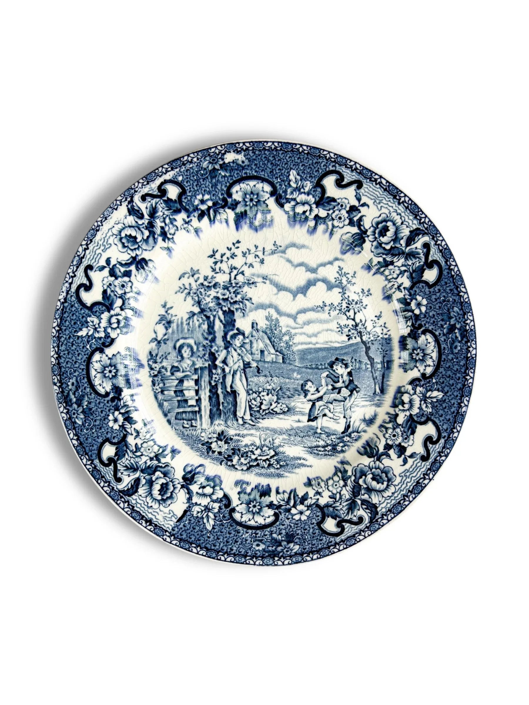 Blue and white vintage ceramic plate with floral border and countryside scene with children playing