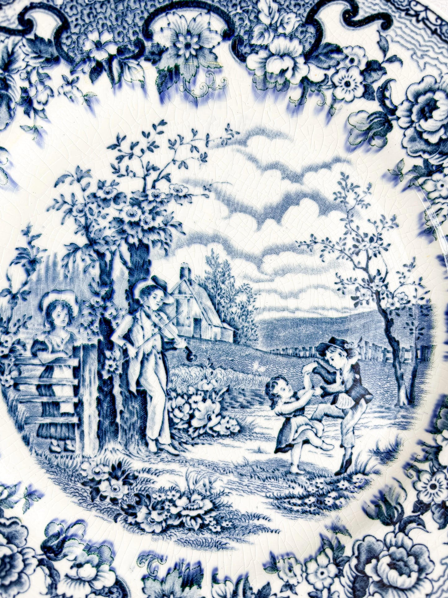 Vintage blue and white ceramic plate with pastoral scene of children dancing and fiddler, floral border