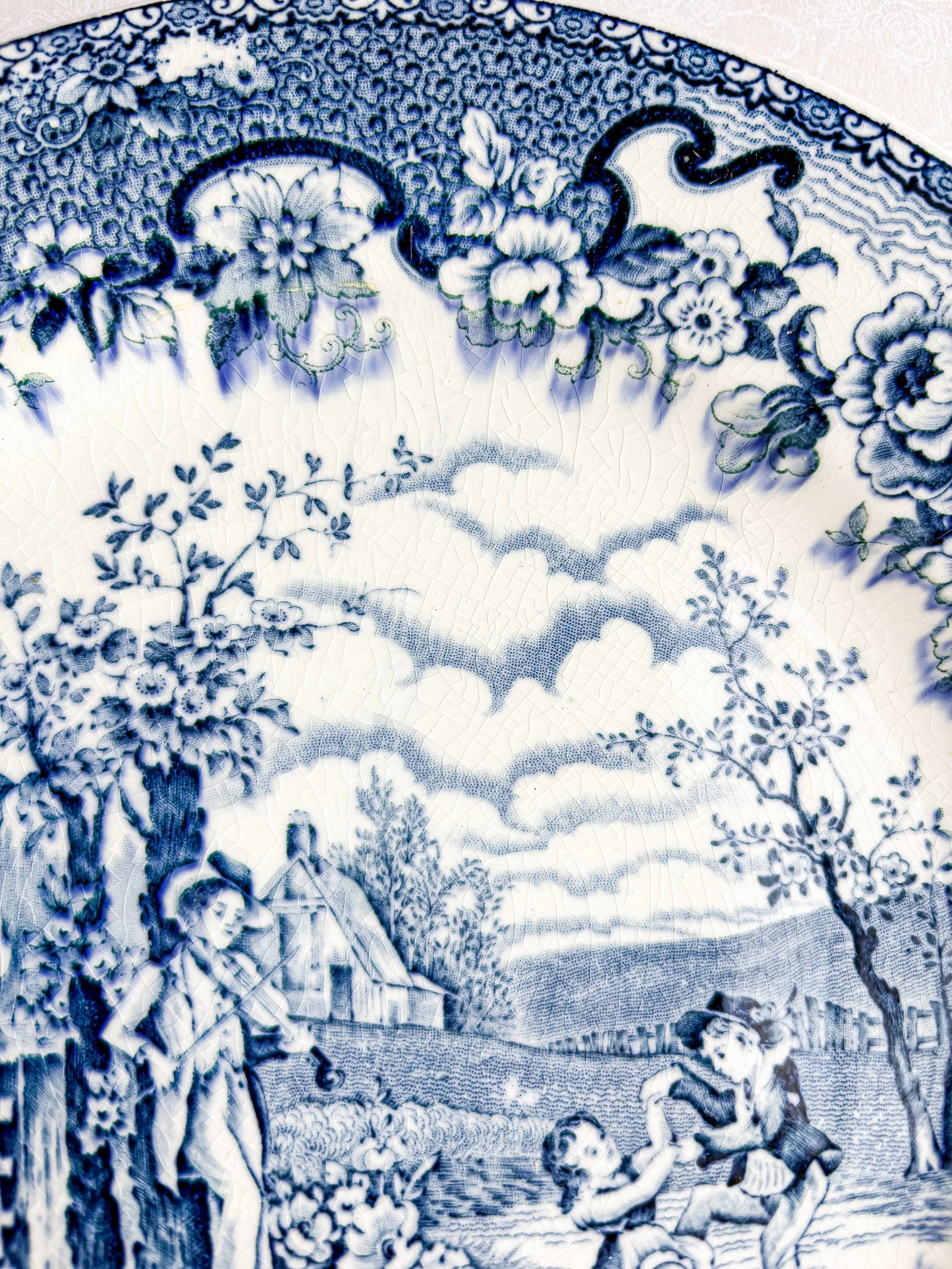 Blue and white vintage porcelain plate with floral border and countryside scene of children and a man playing violin