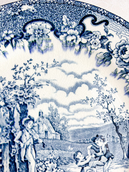 Blue and white vintage porcelain plate with floral border and countryside scene of children and a man playing violin