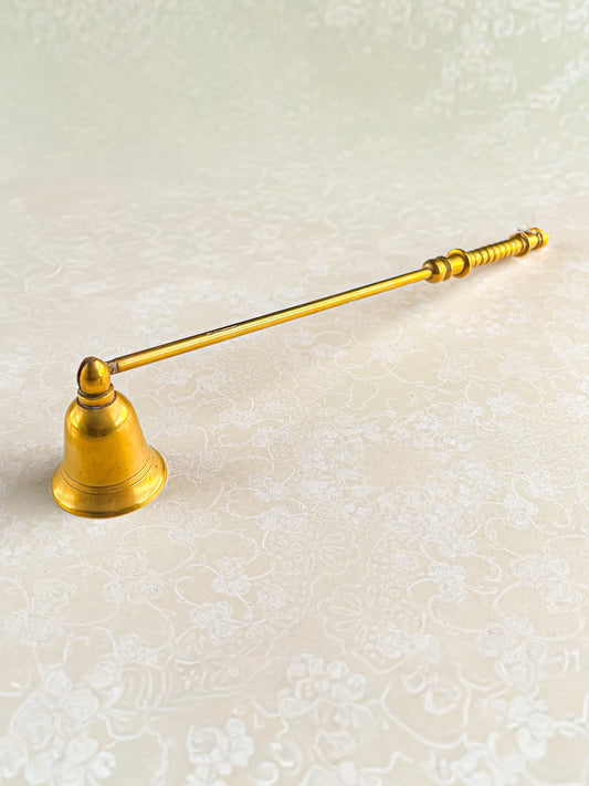 Vintage brass candle snuffer with long handle on patterned light surface