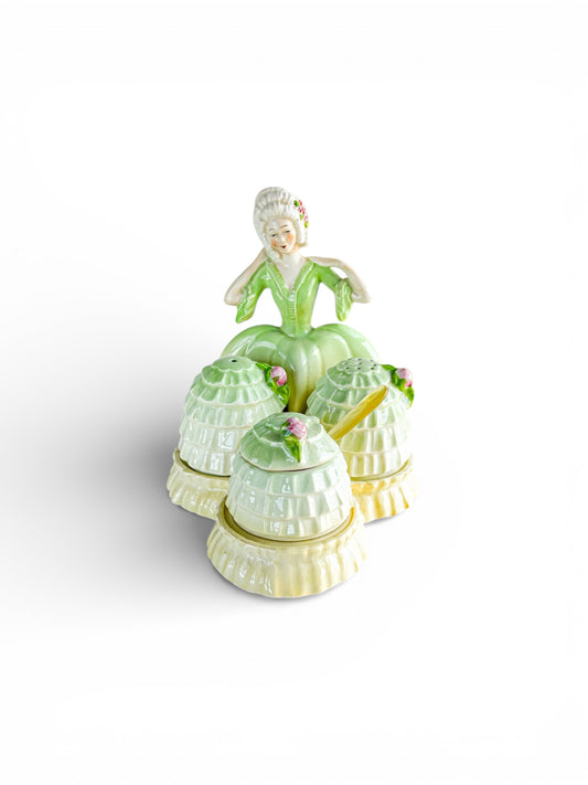 Vintage porcelain condiment set featuring a lady figure in a green dress with matching lidded containers and spoon