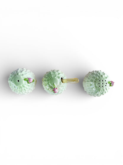 Top view of three light green porcelain condiment containers with pink flower handles on white background