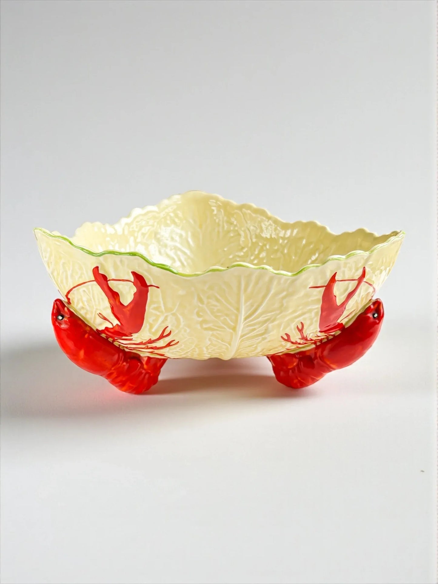 Decorative ceramic bowl shaped like lettuce with red lobster legs as stand, white background