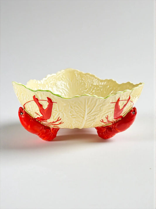 Decorative ceramic bowl shaped like lettuce with red lobster legs as stand, white background
