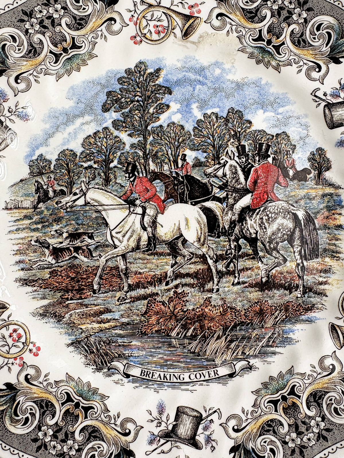 Close-up of the Breaking Cover transfer on a Churchill plate: hunters and hounds leaving woodland cover, a white horse and a spotted grey in the foreground, and the title banner Breaking Cover at the bottom.