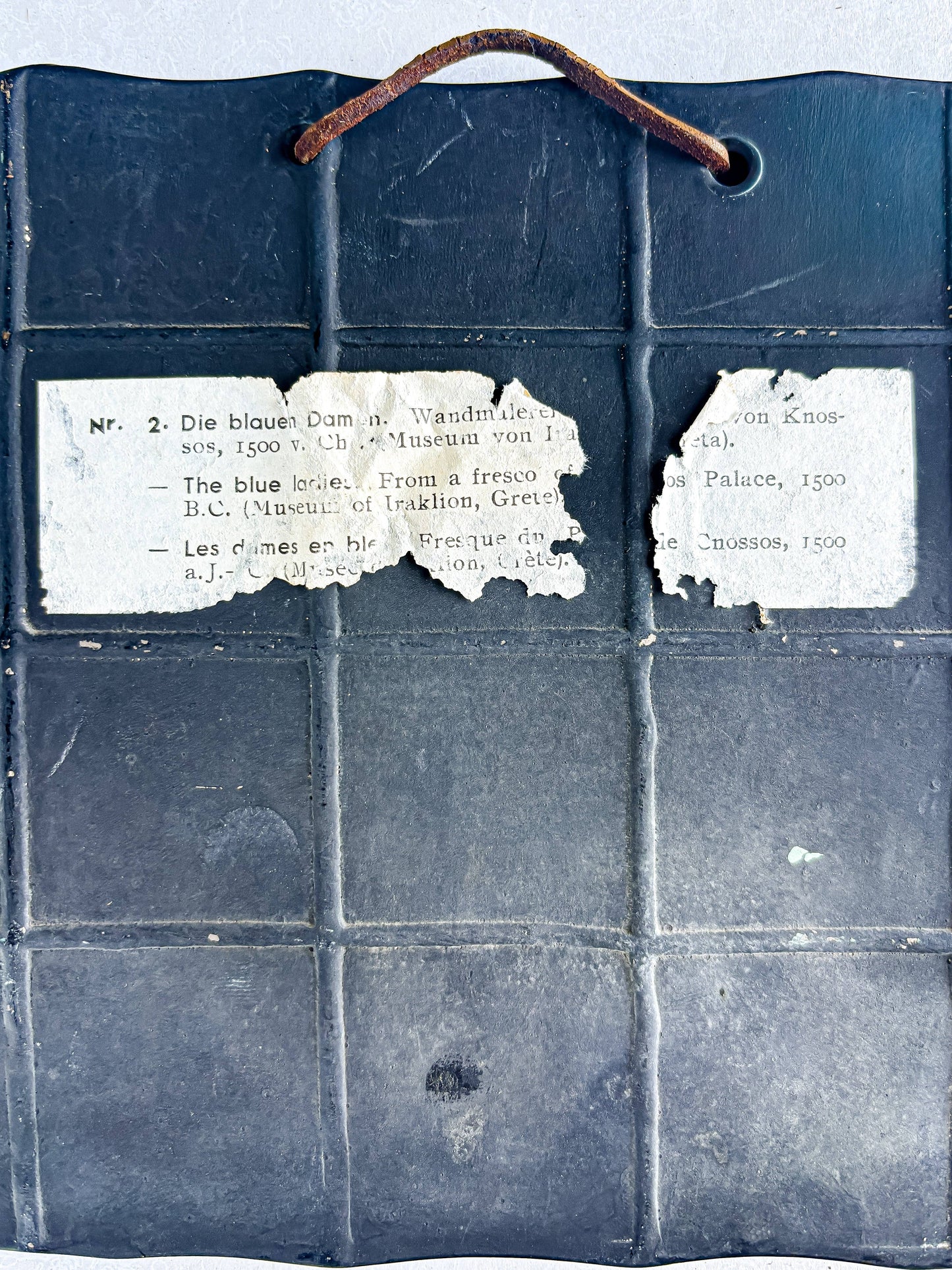 Back of vintage ceramic tile with worn hanging wire and partial paper label about Knossos fresco, collectible tableware.