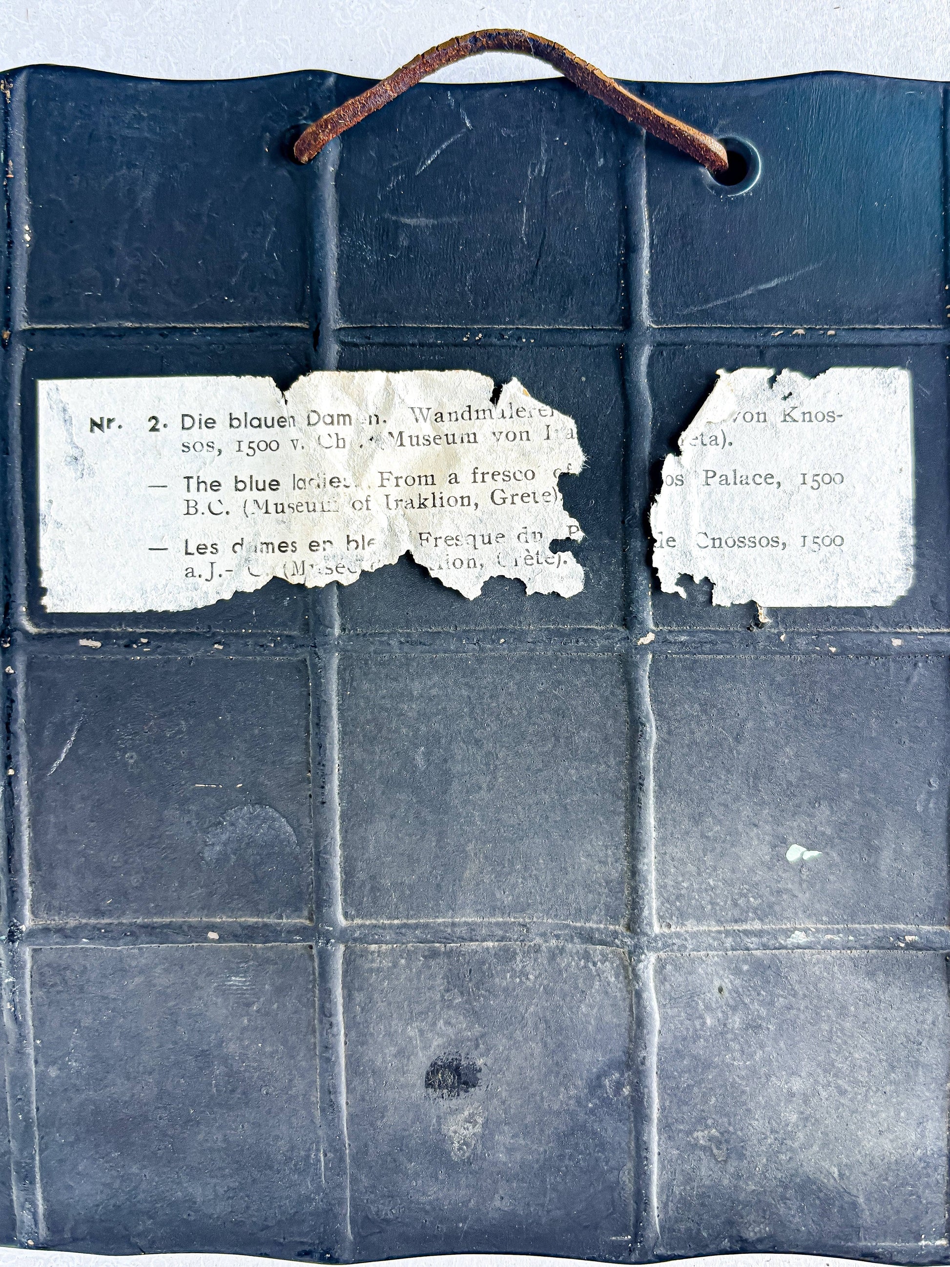 Back of vintage ceramic tile with worn hanging wire and partial paper label about Knossos fresco, collectible tableware.