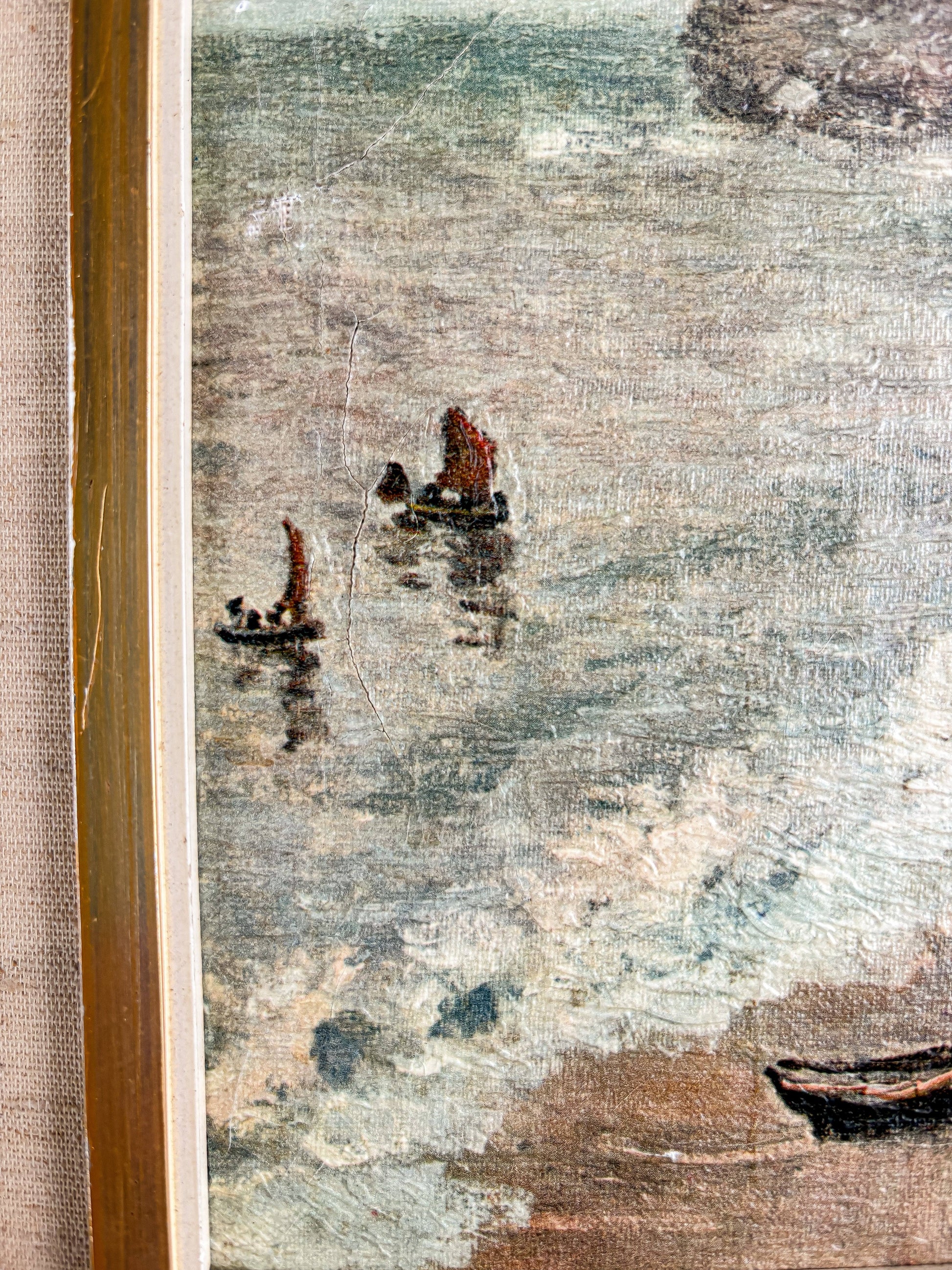 Close-up of framed vintage painting featuring small boats with red sails on textured water near a shoreline