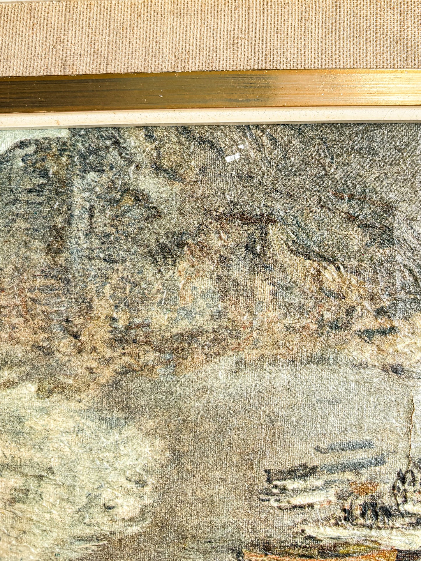 close-up of textured aged canvas painting with muted landscape and gold frame edge