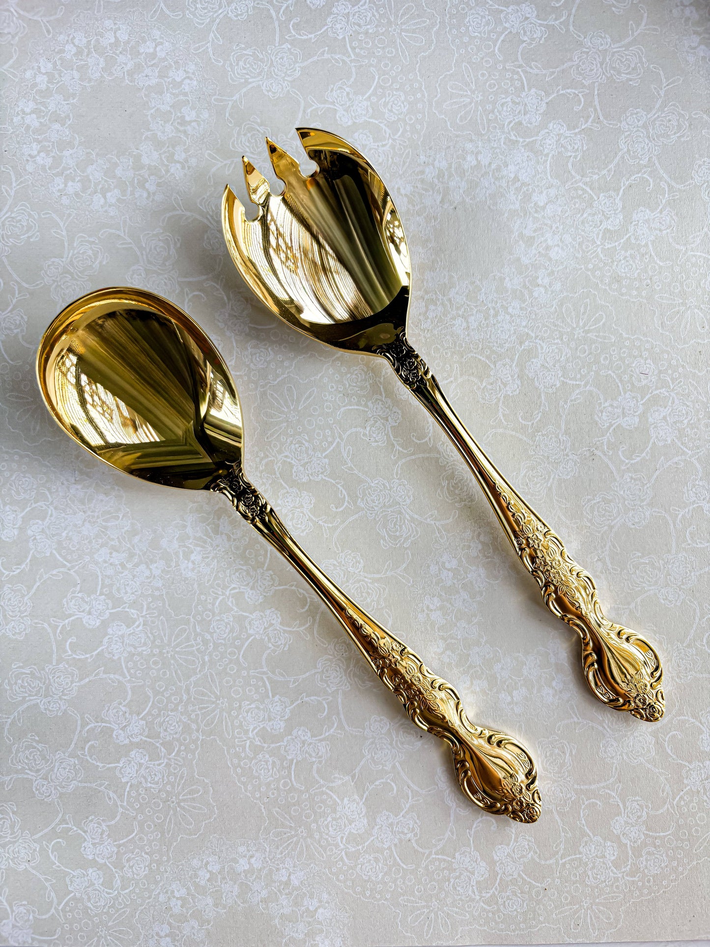 Pair of ornate gold salad serving spoons on floral lace tablecloth