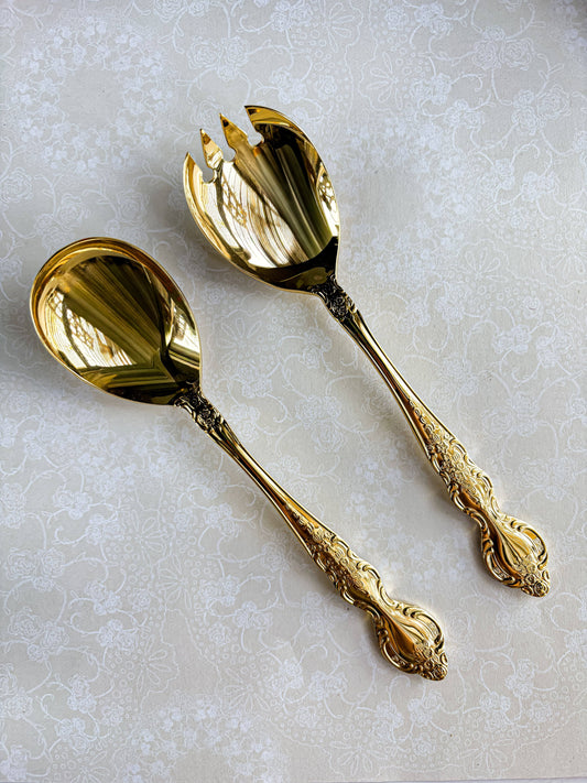 Pair of ornate gold salad serving spoons on floral lace tablecloth