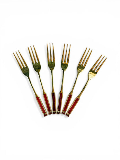 A set of six vintage Eetrite cake forks with 24-carat gold plating and ruby red enamel handles arranged in a fan shape on a white background.