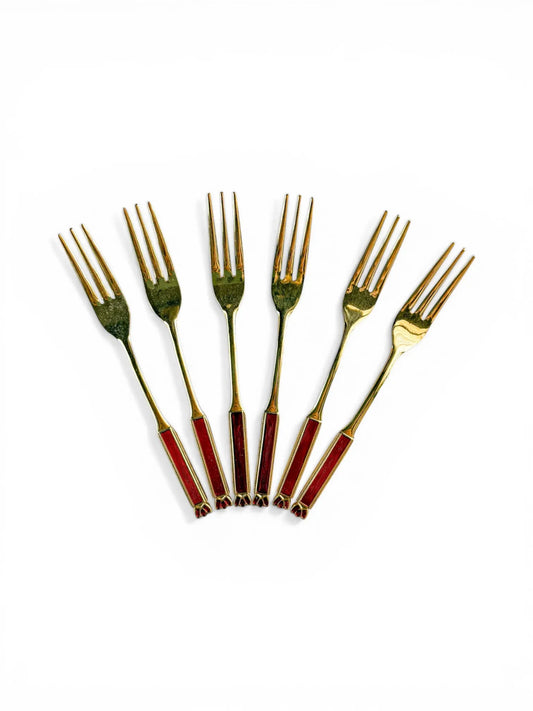 A set of six vintage Eetrite cake forks with 24-carat gold plating and ruby red enamel handles arranged in a fan shape on a white background.