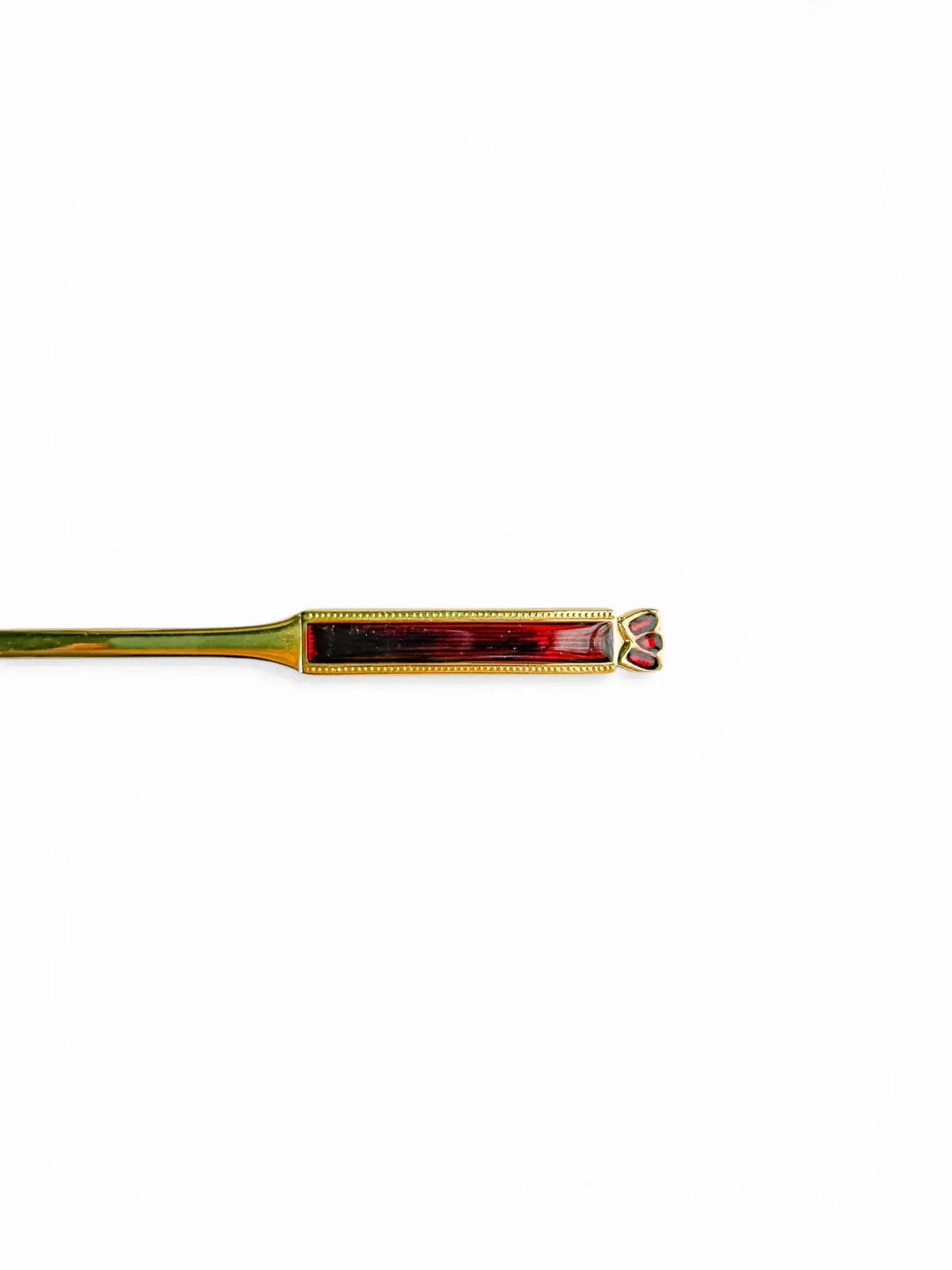Close-up detail of the handle of a vintage Eetrite teaspoon, showing the guilloché-style ruby red enamel and the delicate gold-plated trilobe motif at the tip.
