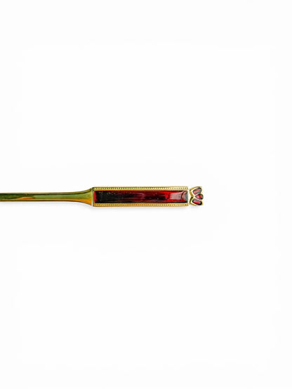 Close-up detail of the handle of a vintage Eetrite teaspoon, showing the guilloché-style ruby red enamel and the delicate gold-plated trilobe motif at the tip.