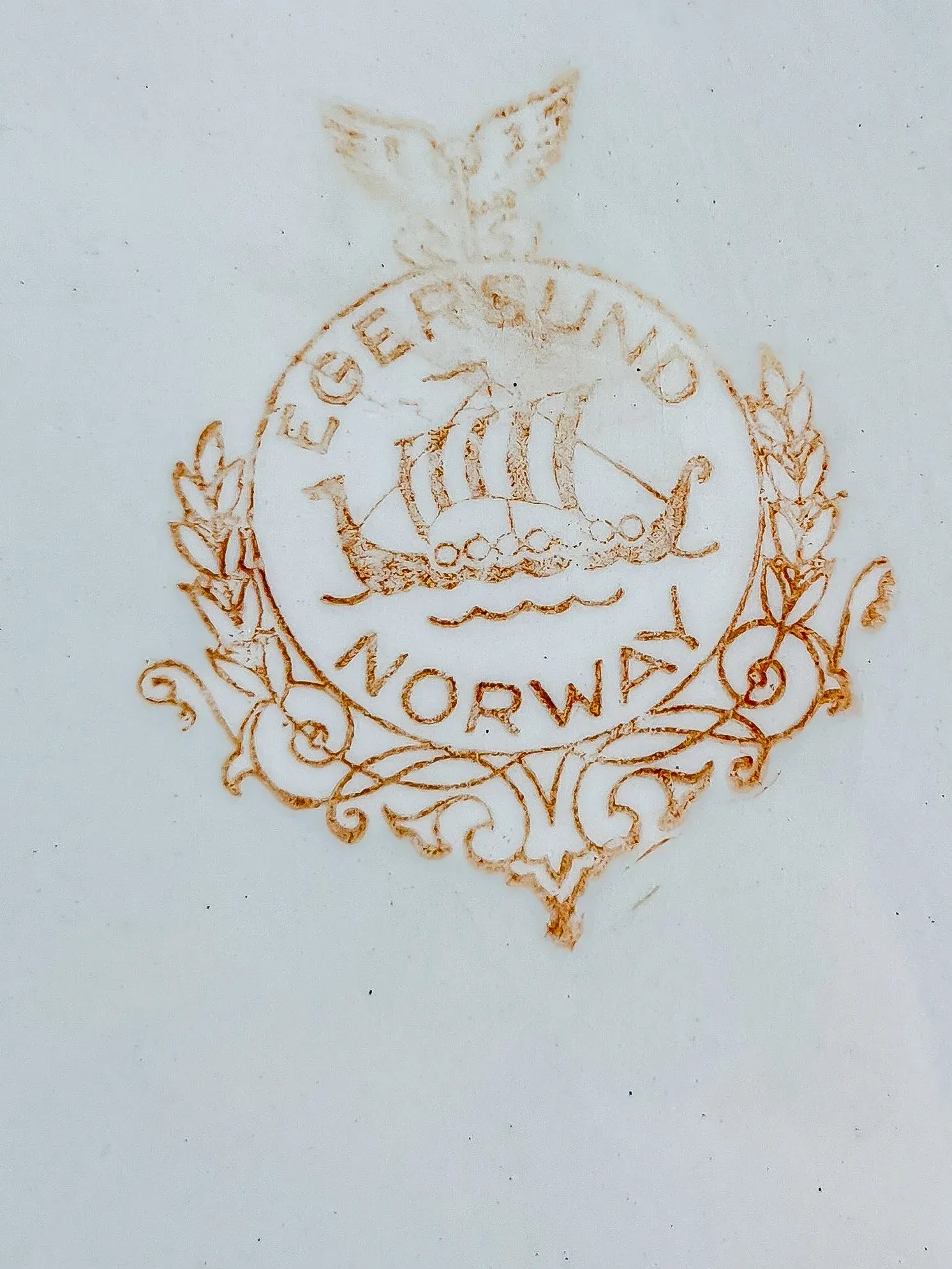 Close-up of the authentic Egersund Norway backstamp on the underside of a ceramic dish, featuring the iconic Viking longship logo in a circular wreath.
