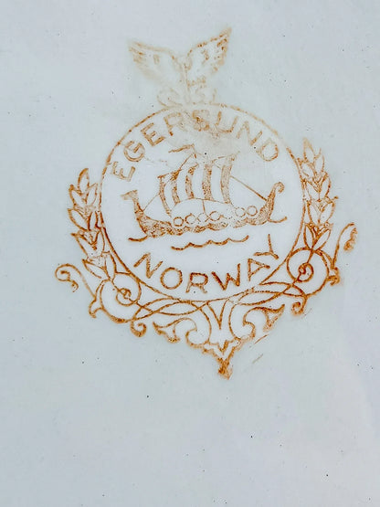 Close-up of the authentic Egersund Norway backstamp on the underside of a ceramic dish, featuring the iconic Viking longship logo in a circular wreath.