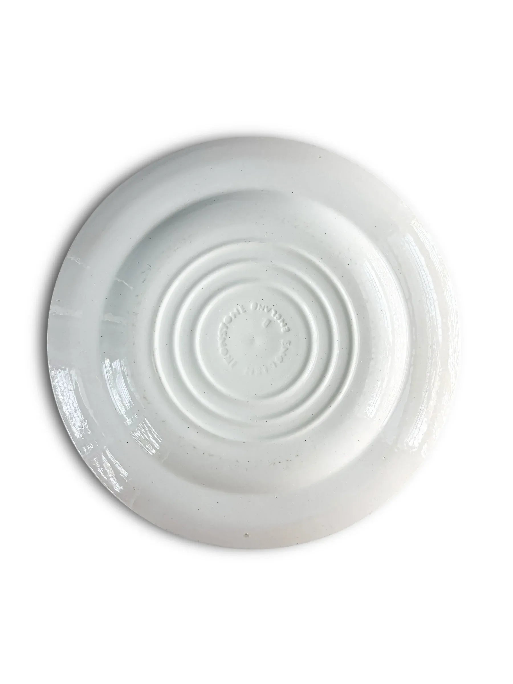 White ceramic plate with concentric circles and embossed text on the back on a white background