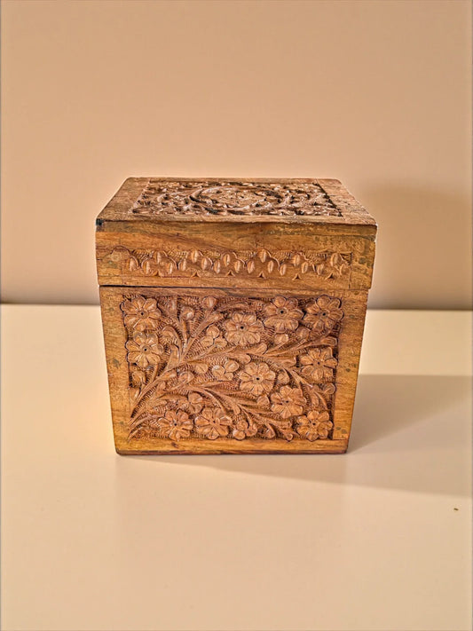Hand-carved wooden box with floral and leaf patterns on beige surface
