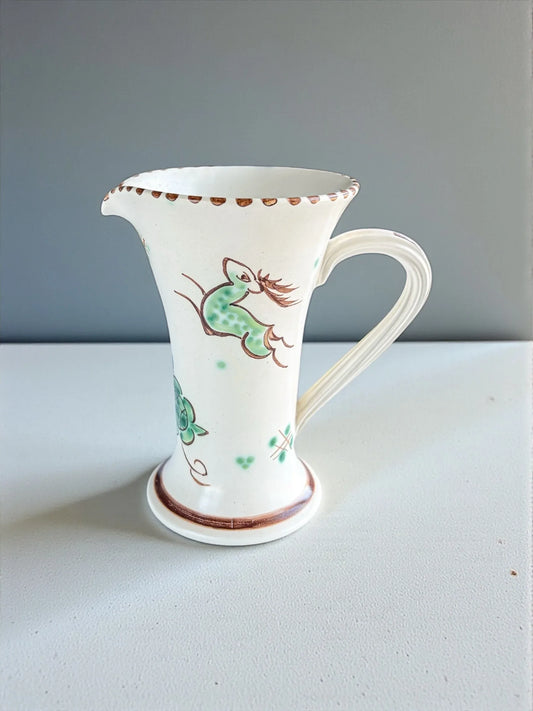 White ceramic pitcher with green and brown floral and bird design on white surface and light gray background