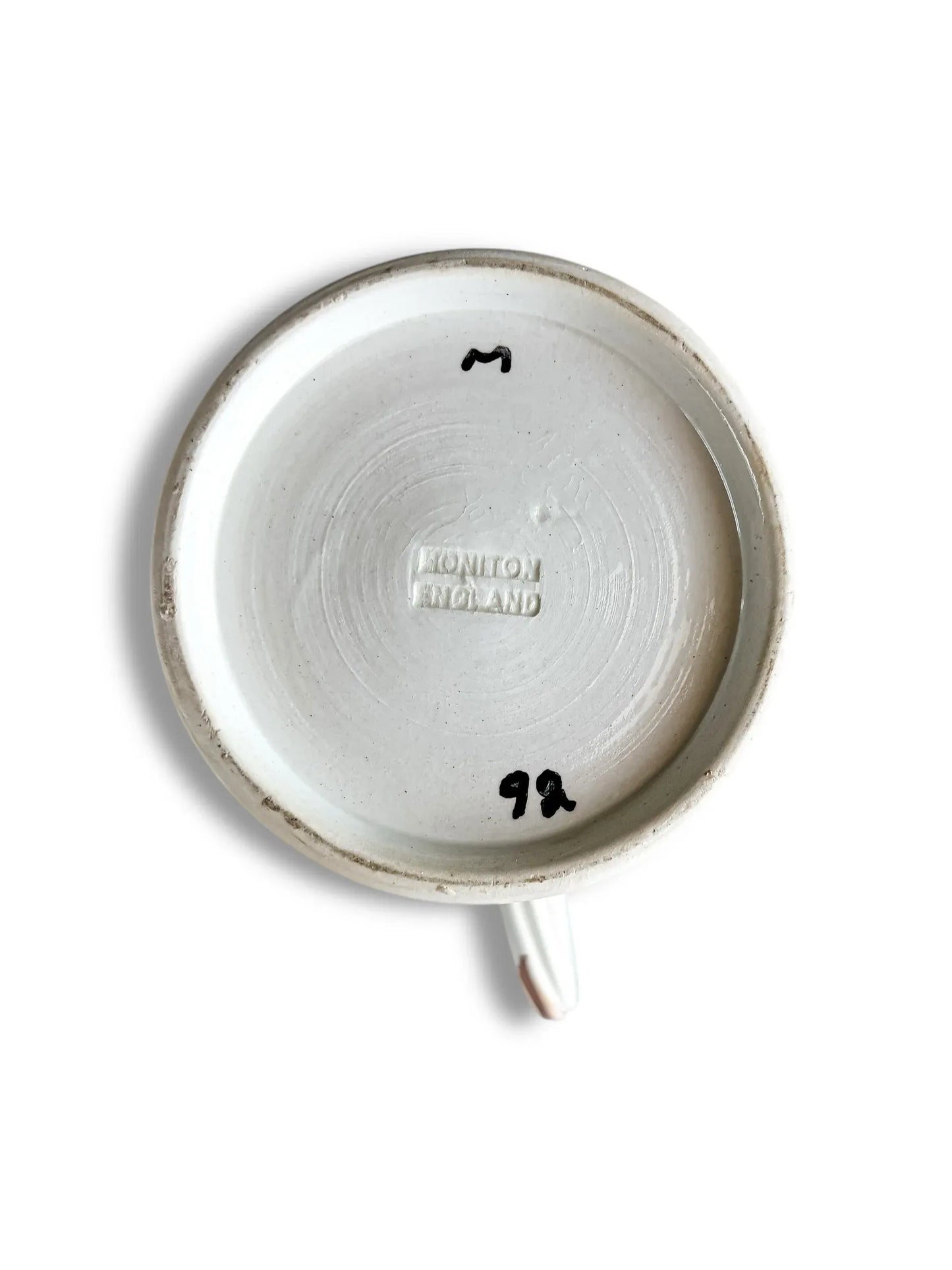 Bottom of a white ceramic cup with embossed text Moniton England and black handwritten markings