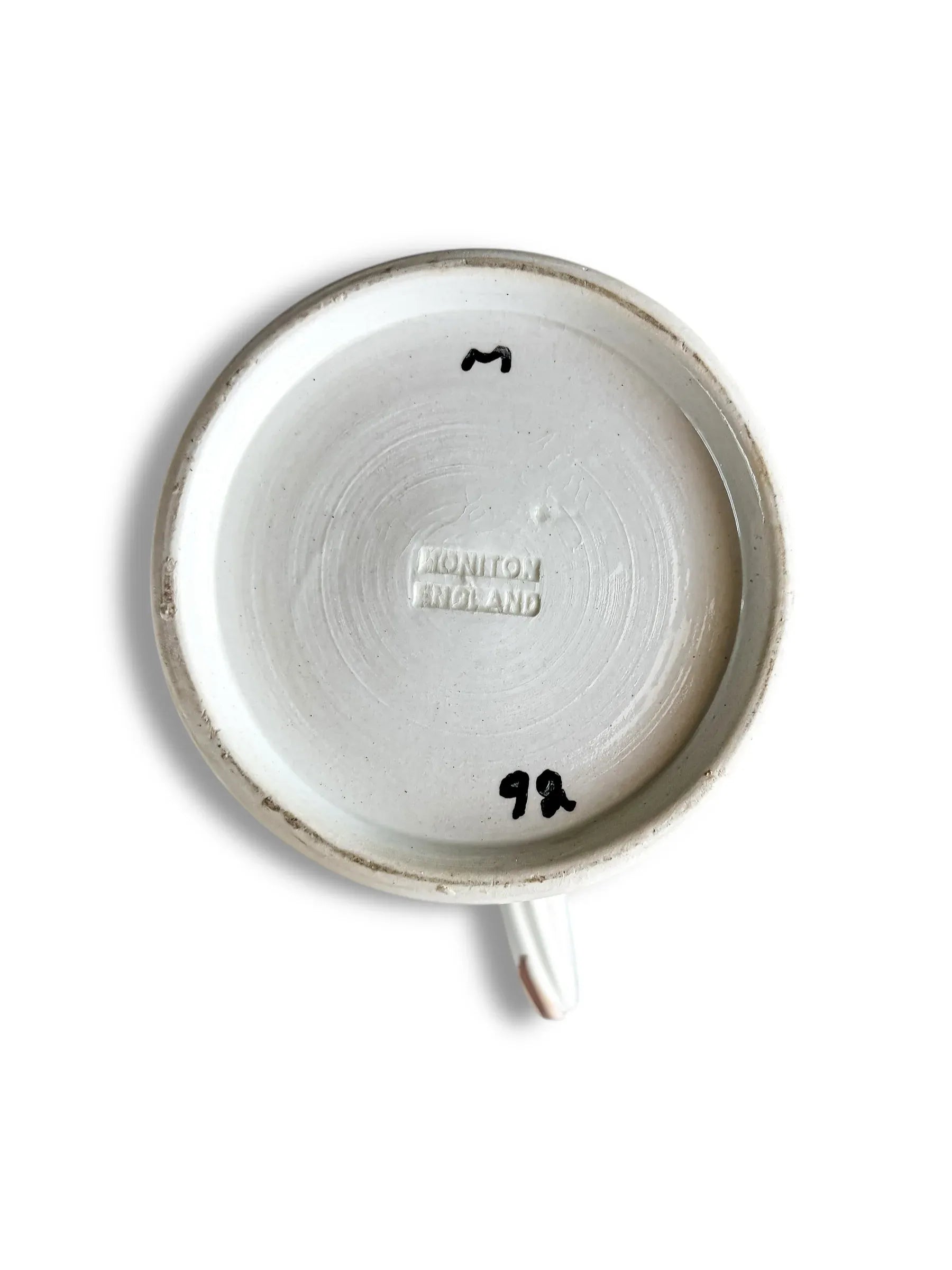 Bottom of a white ceramic cup with embossed text Moniton England and black handwritten markings