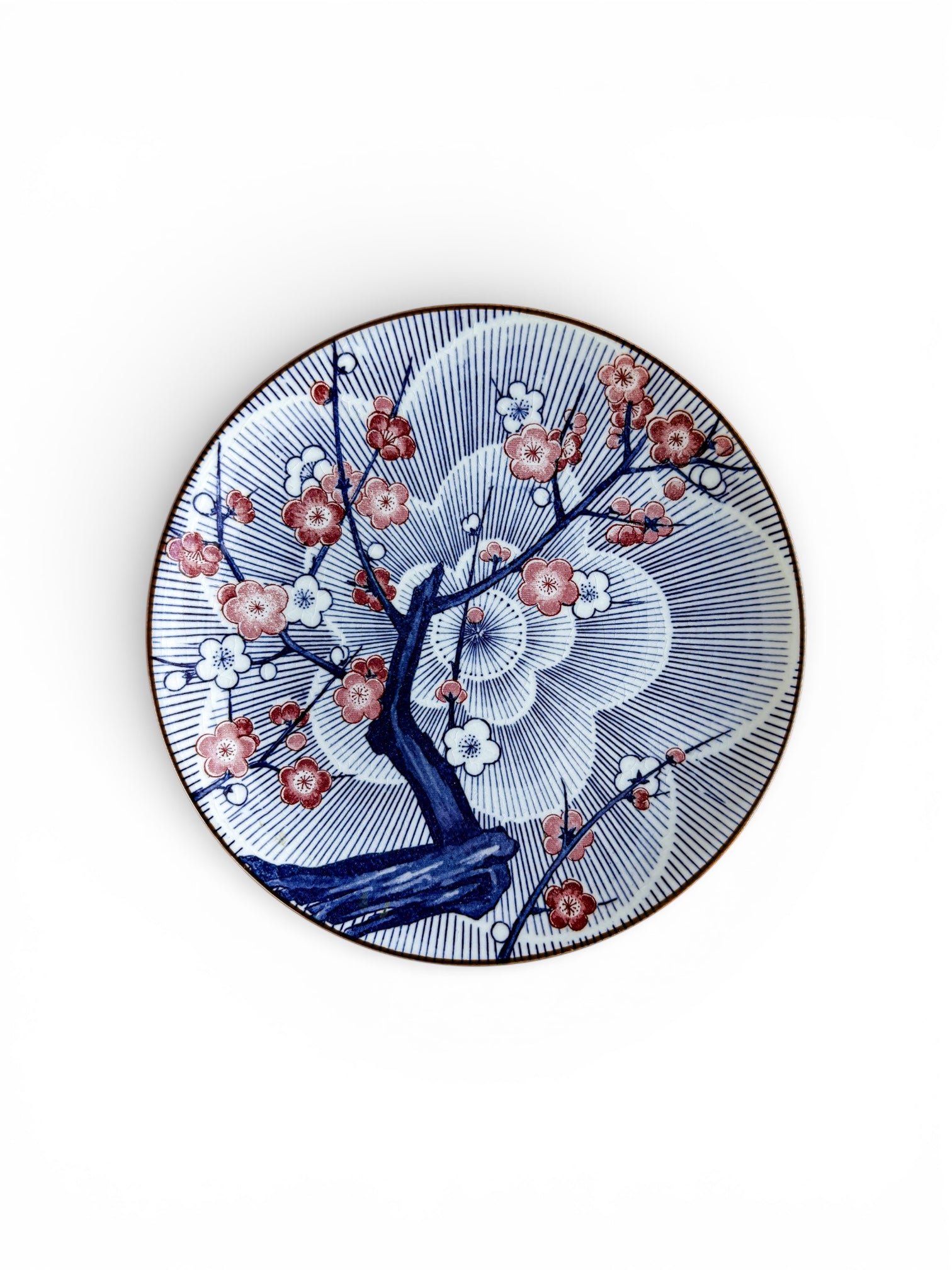 Decorative porcelain plate with blue plum tree and red blossoms, intricate radial pattern background