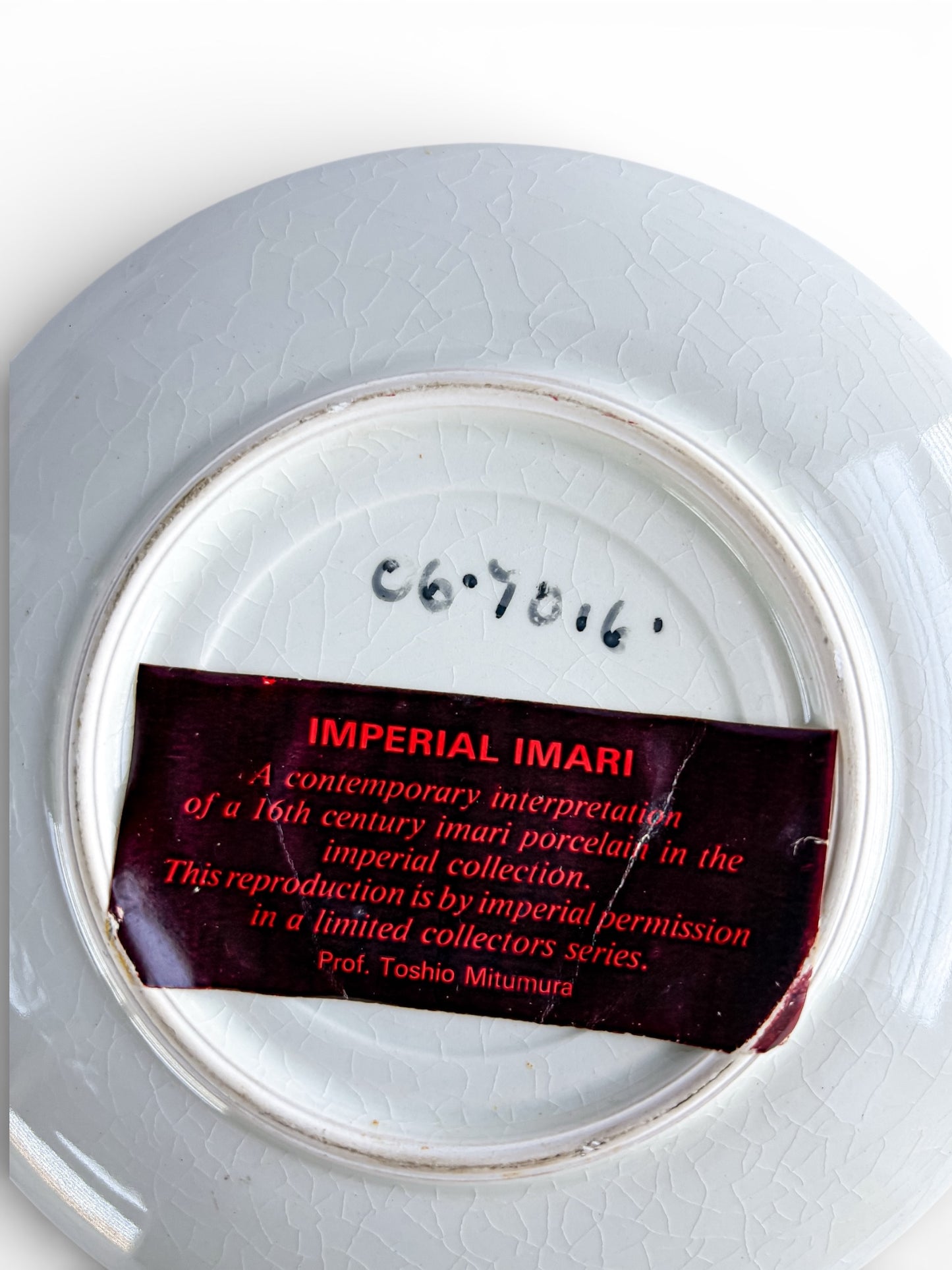 Back of a cracked white porcelain plate with handwritten number and red label reading Imperial Imari limited collectors series