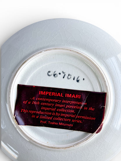 Back of a cracked white porcelain plate with handwritten number and red label reading Imperial Imari limited collectors series