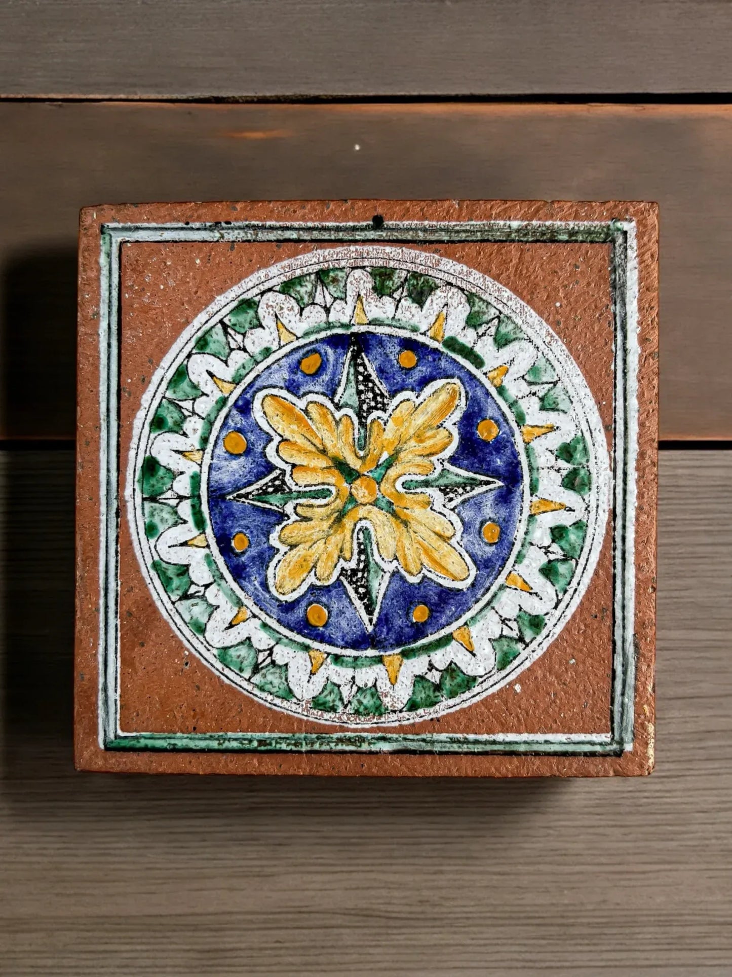 Decorative ceramic tile with blue, yellow, green, and white floral and geometric patterns on wooden surface
