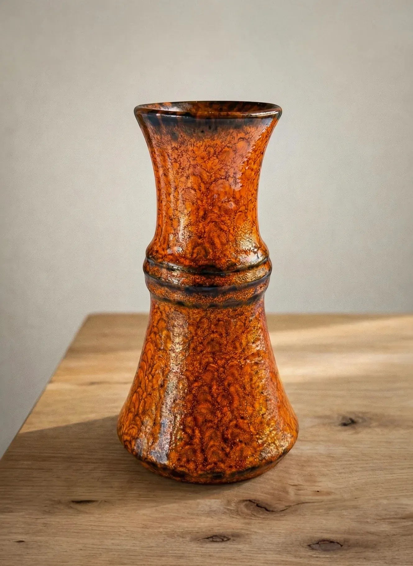 Vintage ceramic vase with orange marbled glaze on wooden table