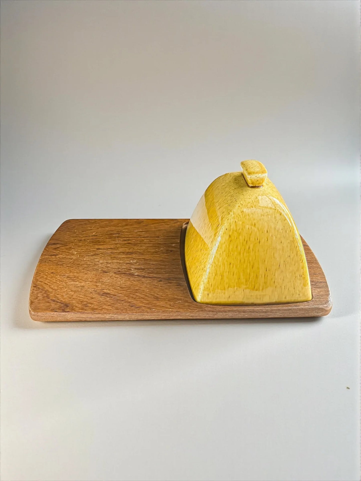 Yellow ceramic butter dish with lid on a rectangular wooden serving board