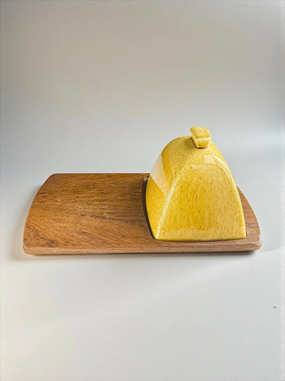Yellow ceramic butter dish with lid on a rectangular wooden serving board
